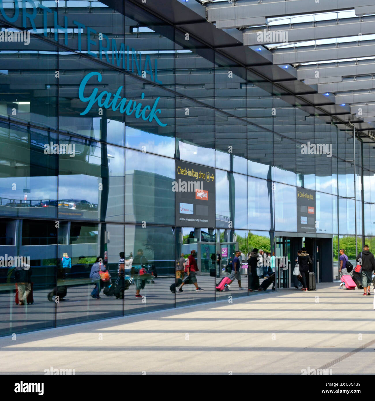 Gatwick Airport North Terminal entrance & sign reflections of airline passengers with suitcase luggage in reflective glass Crawley Sussex England UK Stock Photo