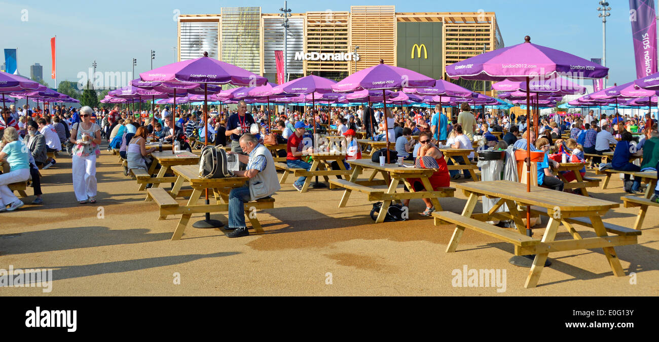 Picnic benches and parasols in the London 2012 Olympic Park with temporary McDonalds store beyond Stock Photo