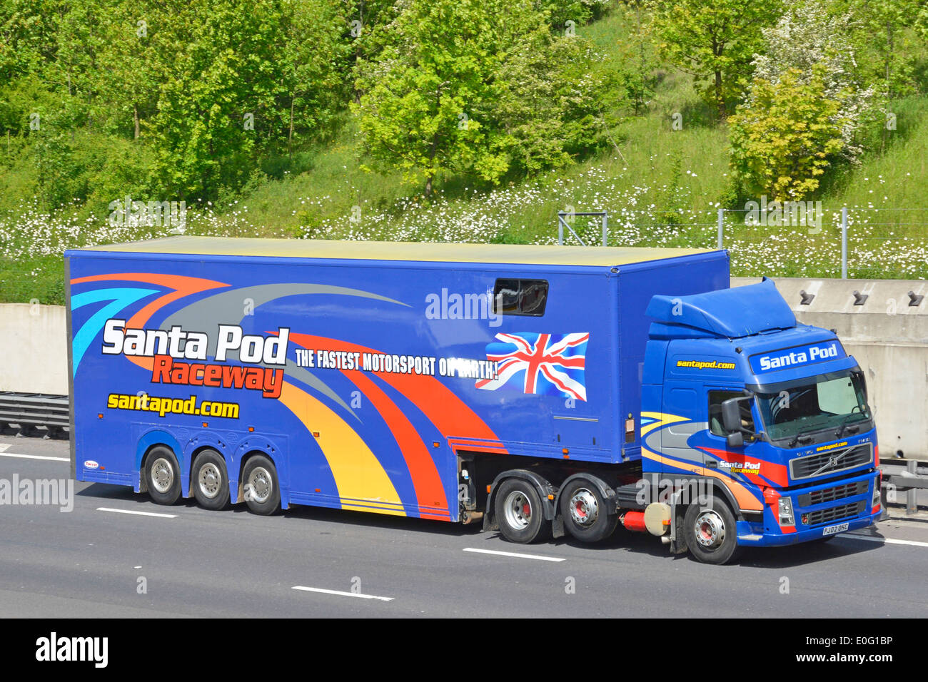 Side & front view of hgv lorry truck with advertising graphics for Santa Pod Raceway on articulated trailer driving along M25 motorway England UK Stock Photo