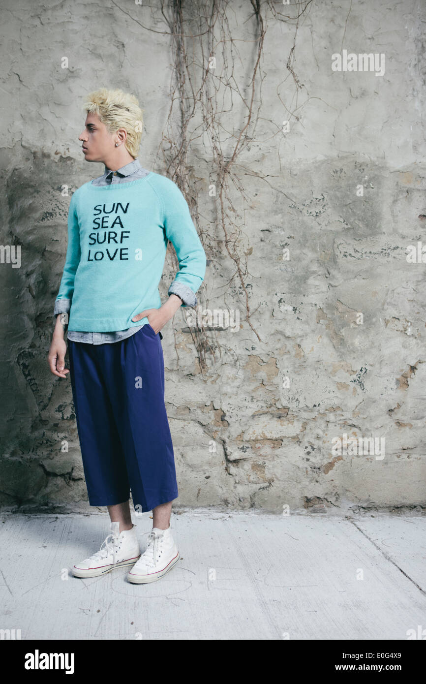Young man in an urban setting, dreaming of the beach and wanting to go there, 'Sun, Sea, Surf, Love' printed on the sweater. Stock Photo
