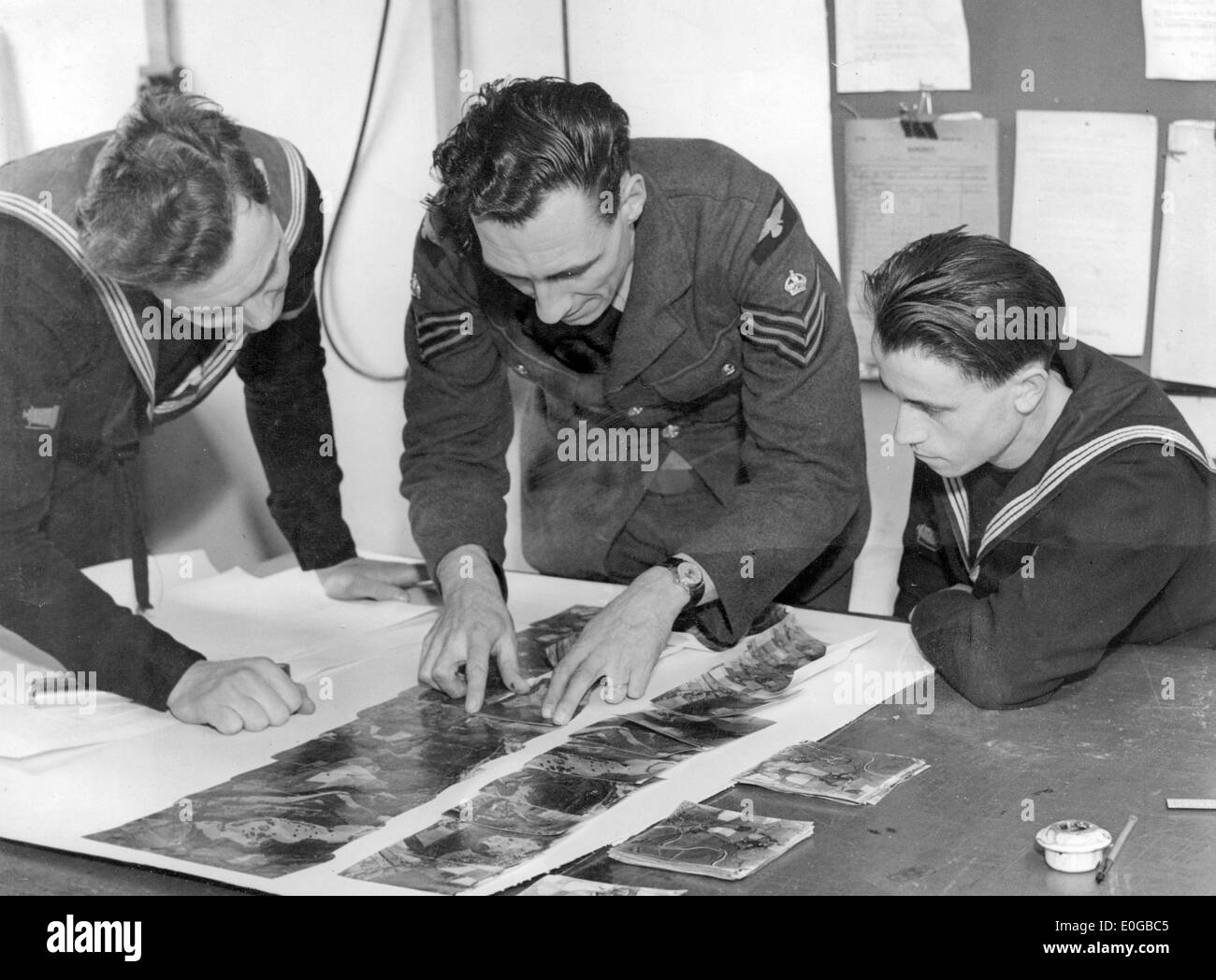 Royal Navy photographers and an RAF sergeant inspect aerial photographs of enemy instalations Stock Photo