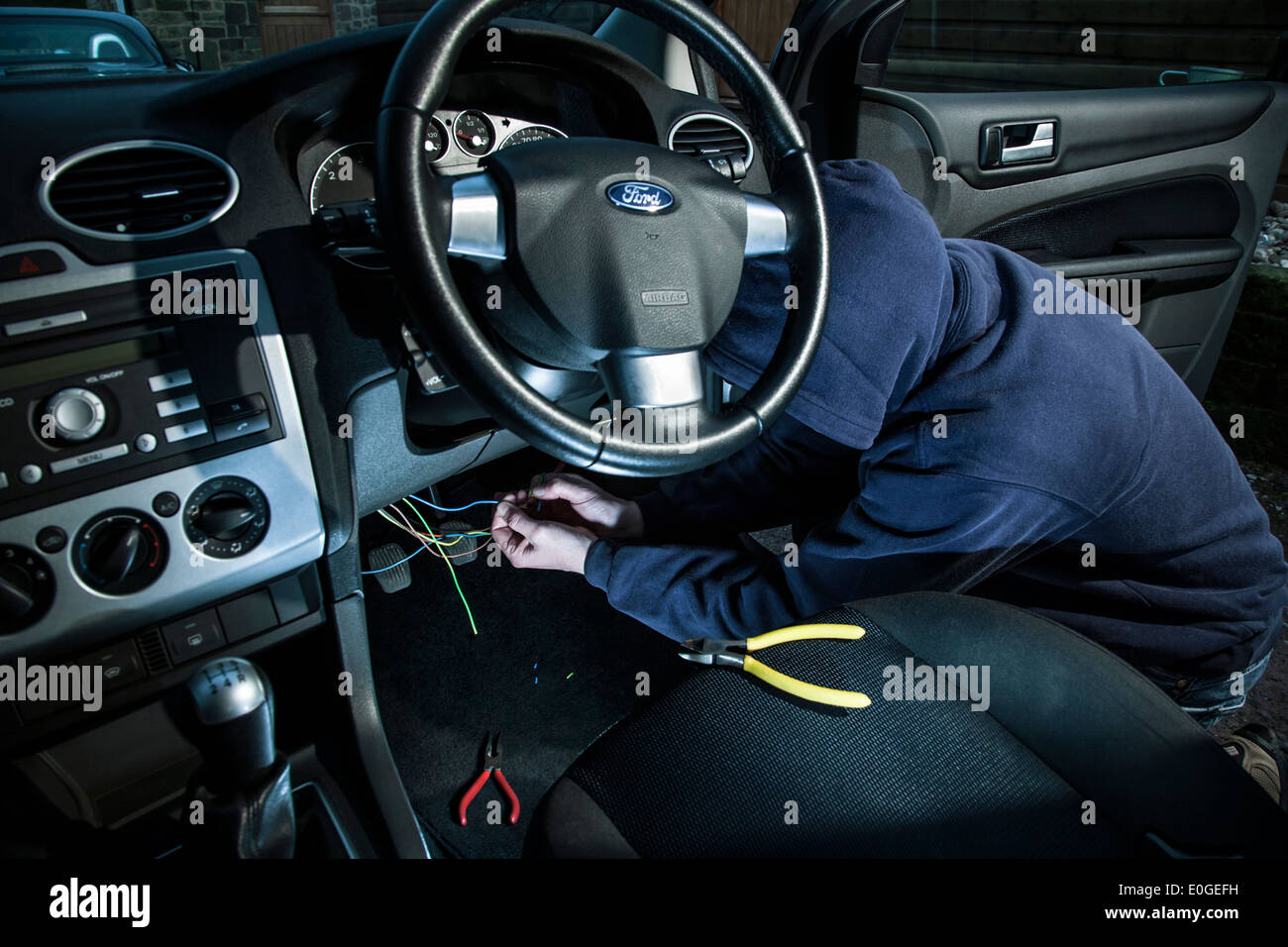 A man wearing a hoody hot wiring a car. Stock Photo