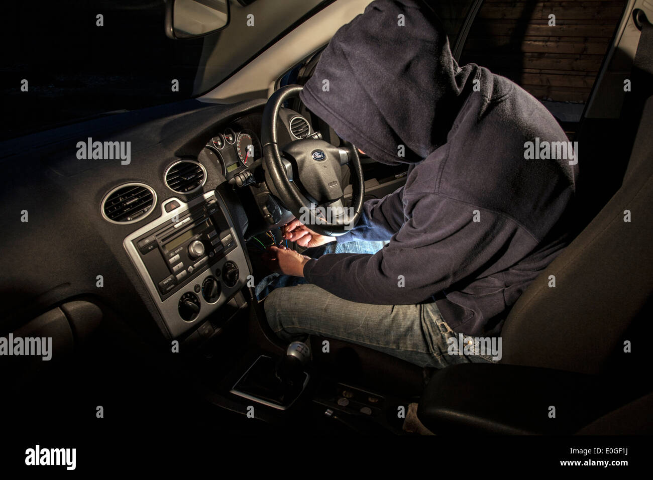 A man wearing a hoody hot wiring a car. Stock Photo