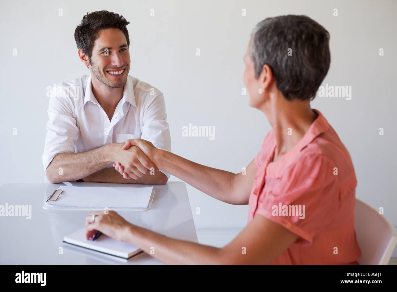 Casual business people shaking hands at desk and smiling Stock Photo