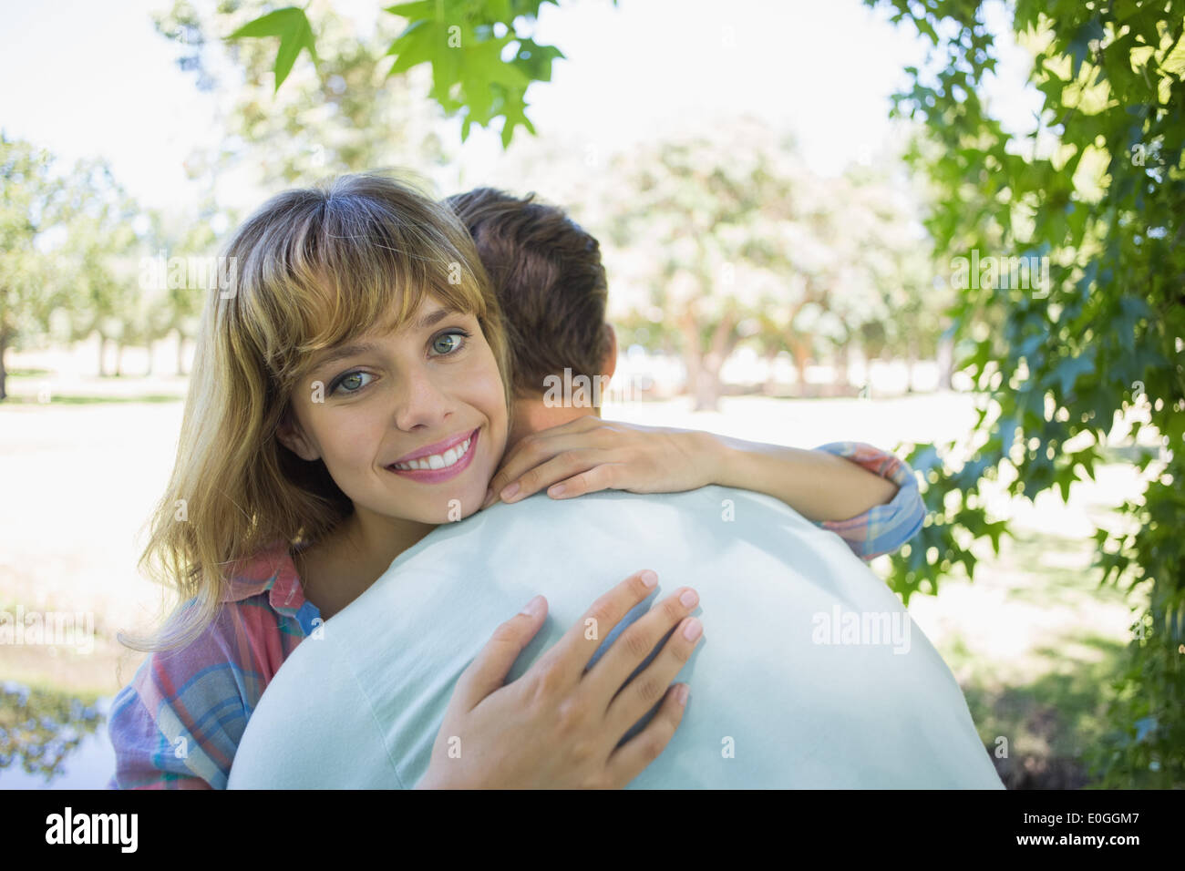 Pretty blonde smiling at the camera in a park while hugging boyfriend ...