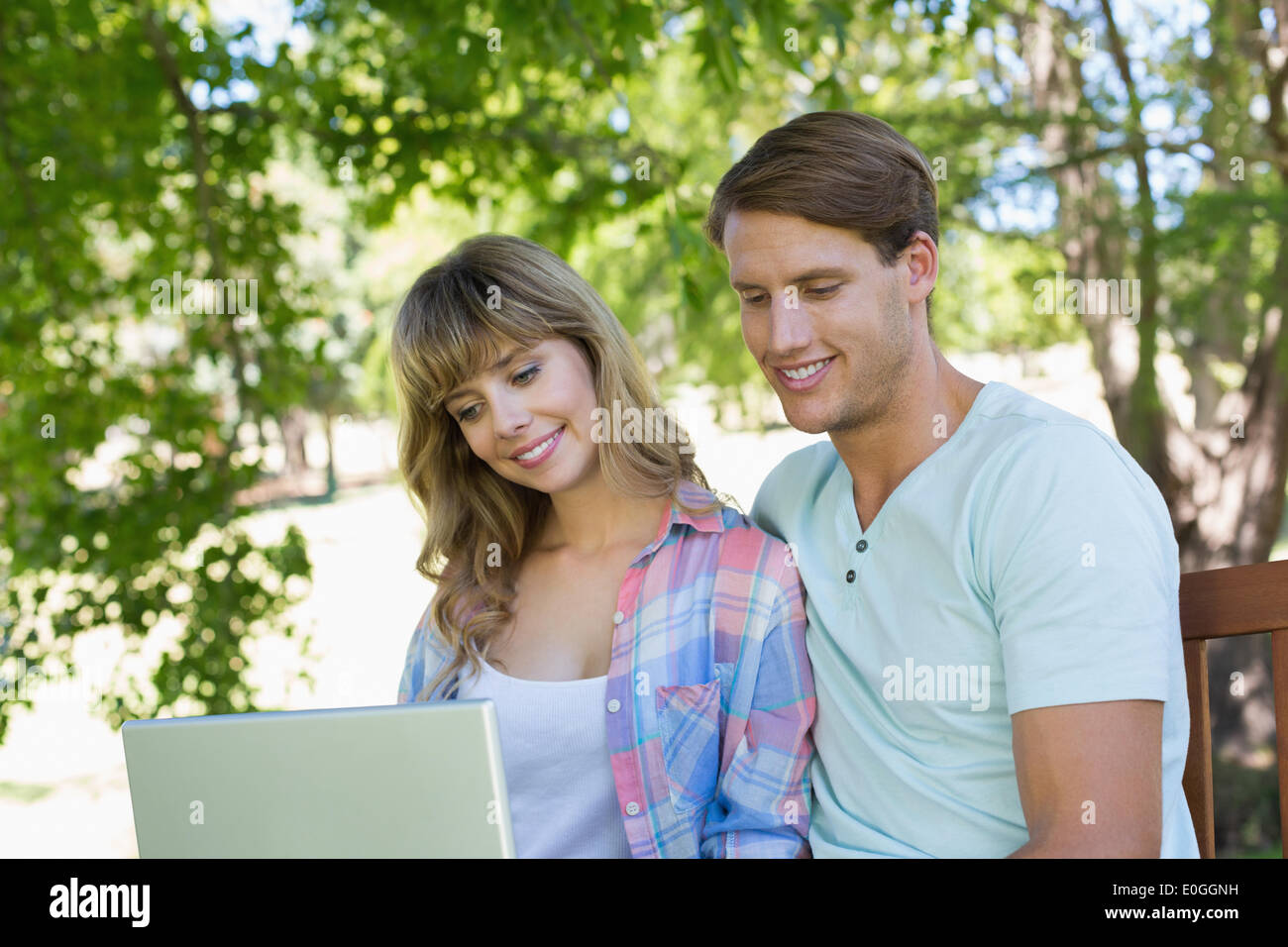 Cute young couple sitting on park bench using laptop Stock Photo - Alamy