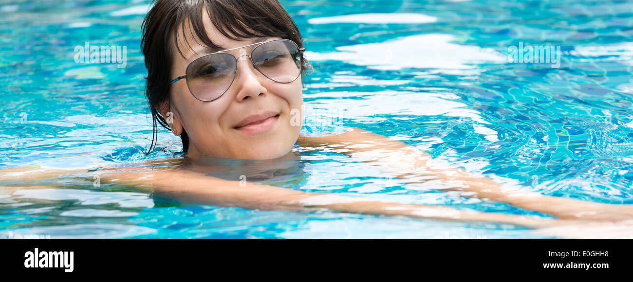 Portrait of a beautiful young woman in sunglasses floating in the pool ...
