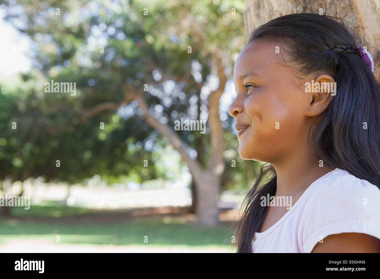 Little girl sitting by tree smiling Stock Photo - Alamy