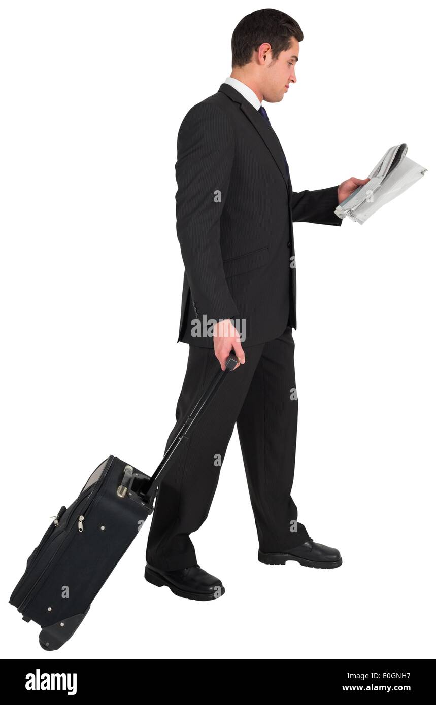 Businessman pulling his suitcase holding newspaper Stock Photo