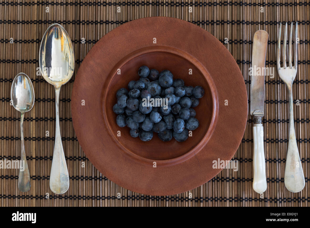 A photograph of some antique silver cutlery and a wooden jarrah bowl filled with blueberries. Stock Photo