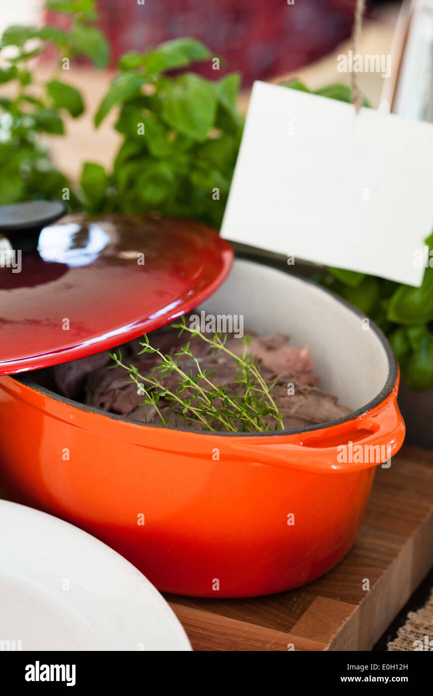 Closeup of pot of cooked beef with decorative herb garnish resting on wooden tray with lid pulled back Stock Photo