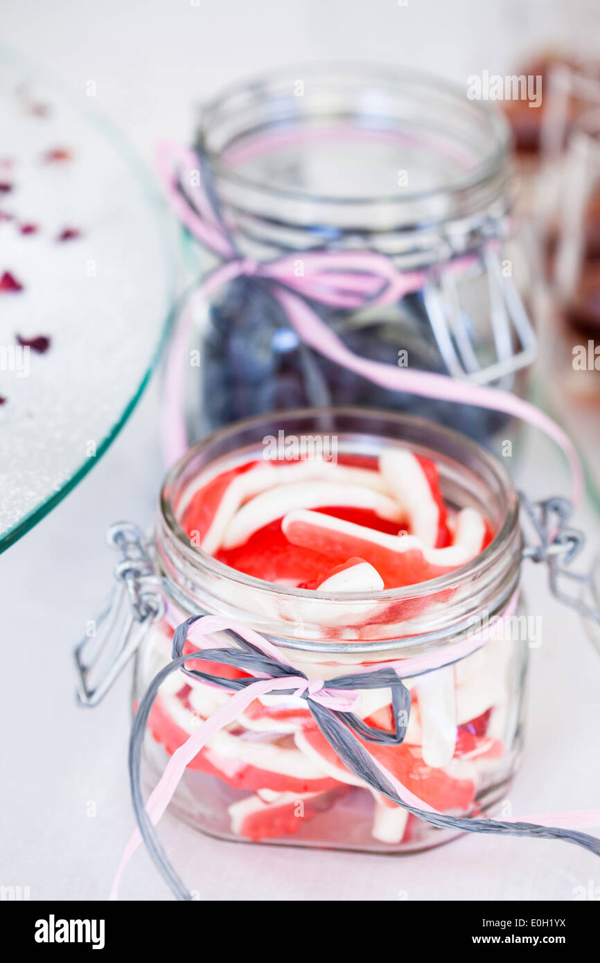 Closeup of soft red and white colored sugary candies in glass jar with decorative ribbon tied in bow Stock Photo