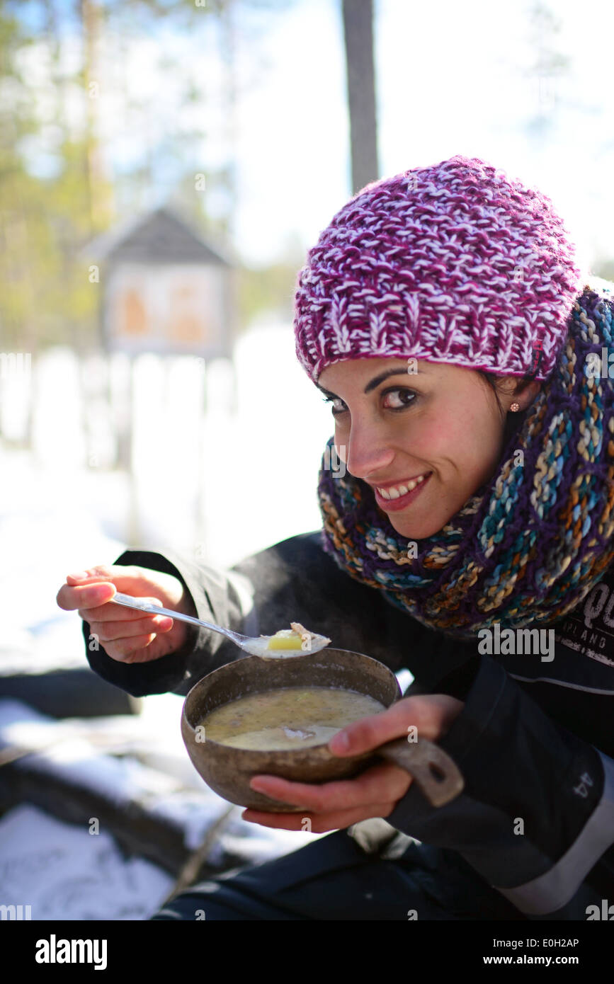 Young woman enjoys a tasty salmon soup. Wilderness husky sledding taiga tour with Bearhillhusky in Rovaniemi, Lapland, Finland Stock Photo