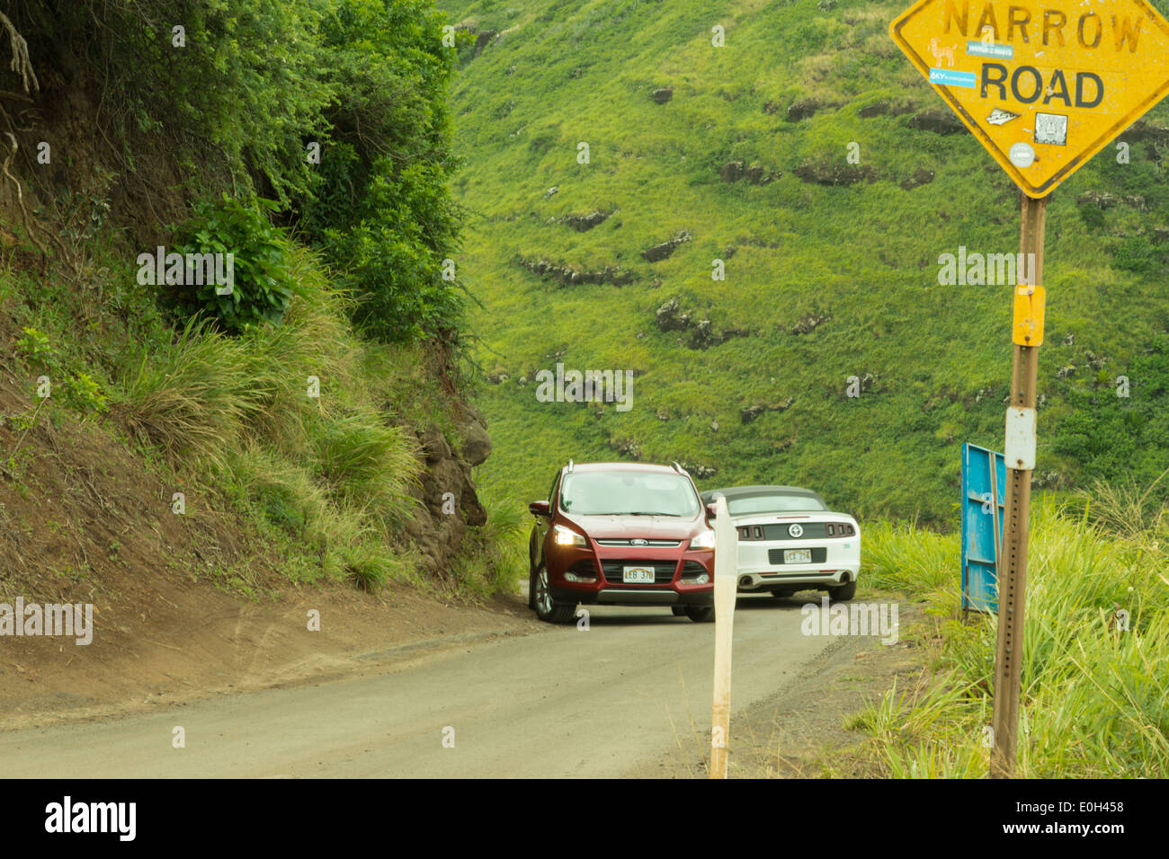 Two cars passing each other on a narrow coastal road in West Maui Stock