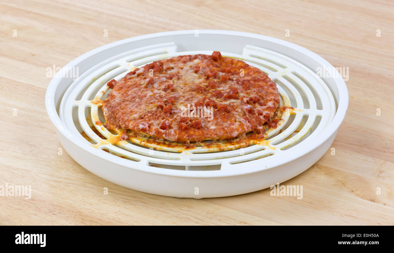 A small pepperoni pizza that has been overly cooked in a microwave atop a wood counter top. Stock Photo