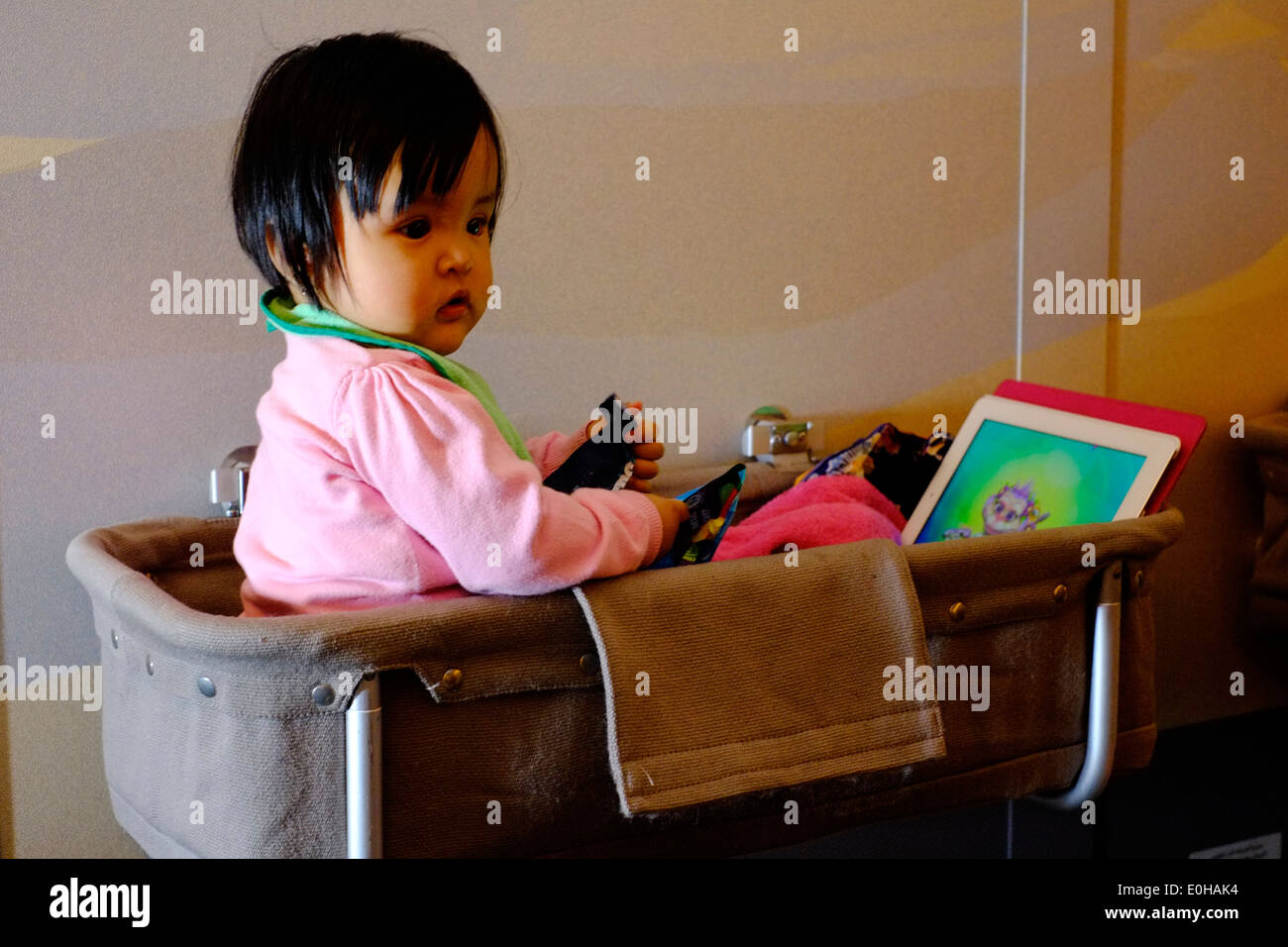 young child sits playing in a bassinet in economy class on board an airbus flight Photo - Alamy
