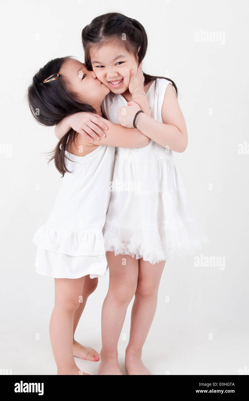 Little girls portrait. Asian sisters kissing on plain background. Sibling love. Stock Photo