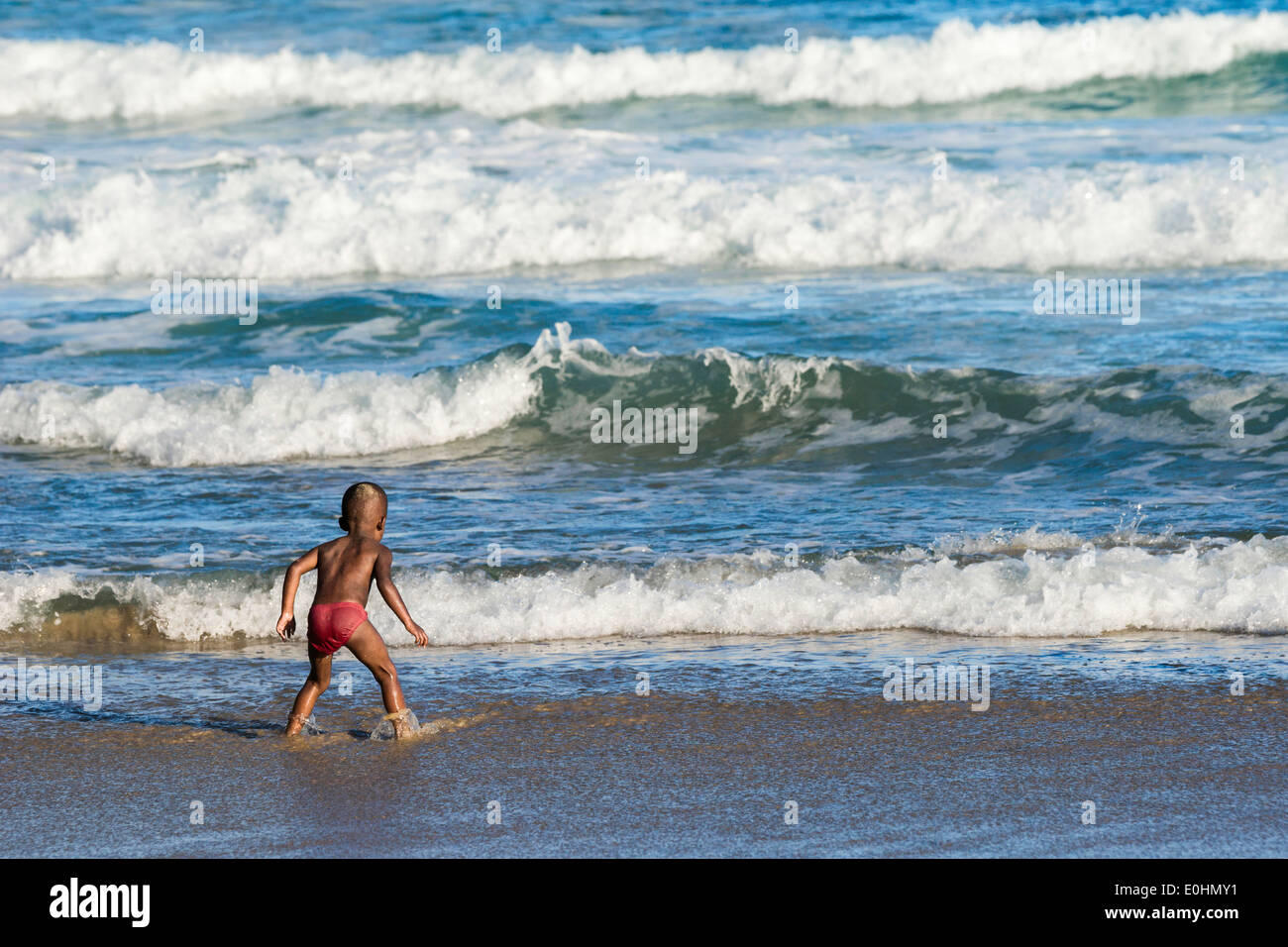 Young boy braces himself in shallow waters as he watches and waits for giant  waves to approach shore in the Indian Ocean Stock Photo - Alamy