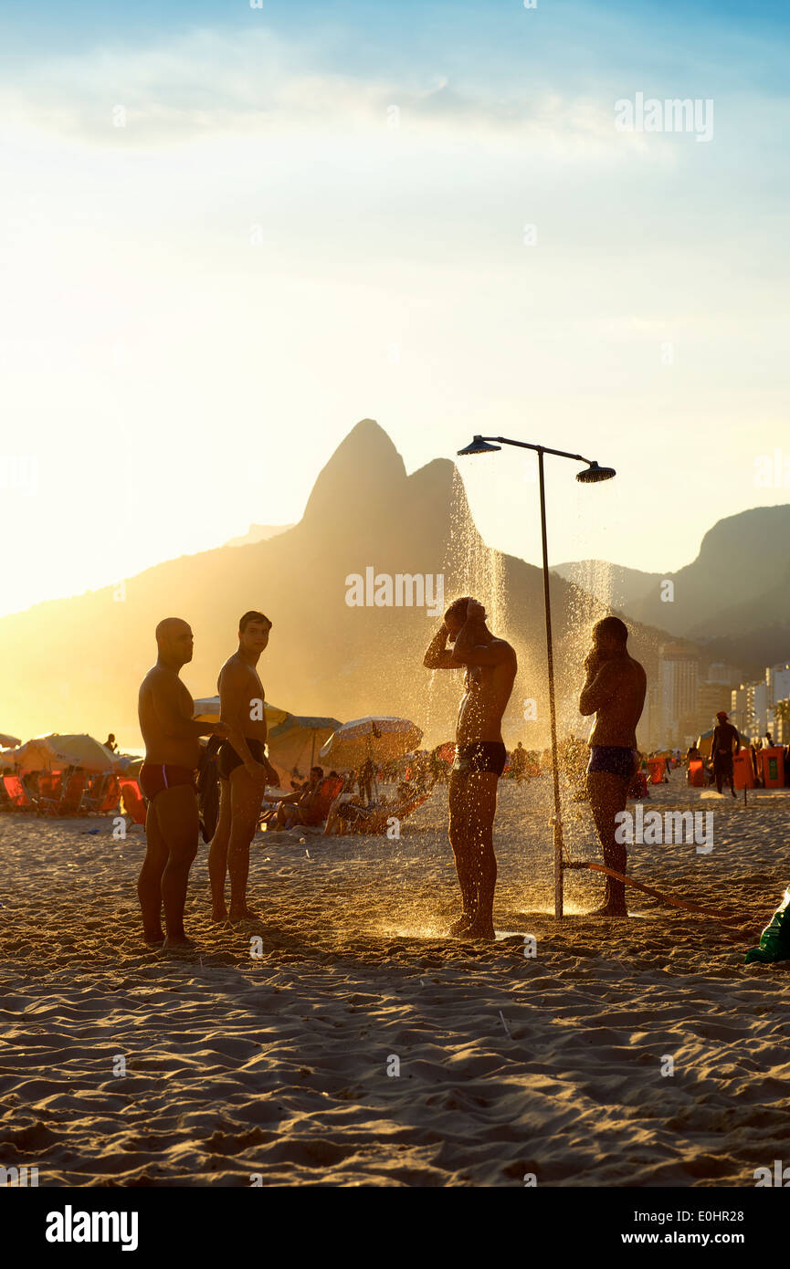 RIO DE JANEIRO, BRAZIL - JANUARY 25, 2014: Group of Brazilian men stand under the outdoor showers on Ipanema Beach at sunset. Stock Photo