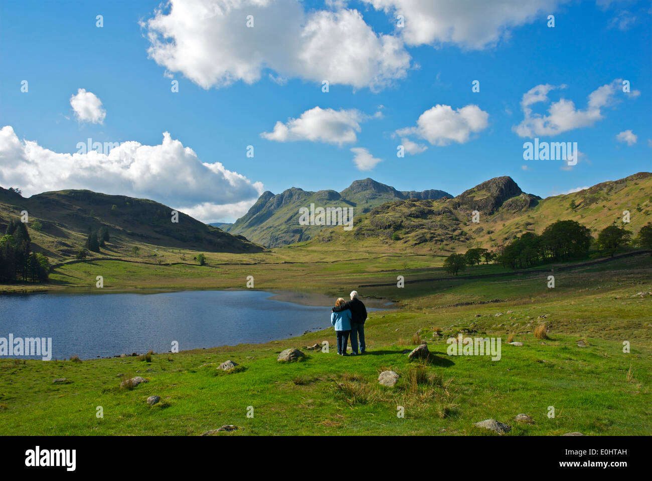 Couple looking beyond Blea Tarn to the Langdale Pikes, Little Langdale, Lake District National Park, Cumbria, England UK Stock Photo