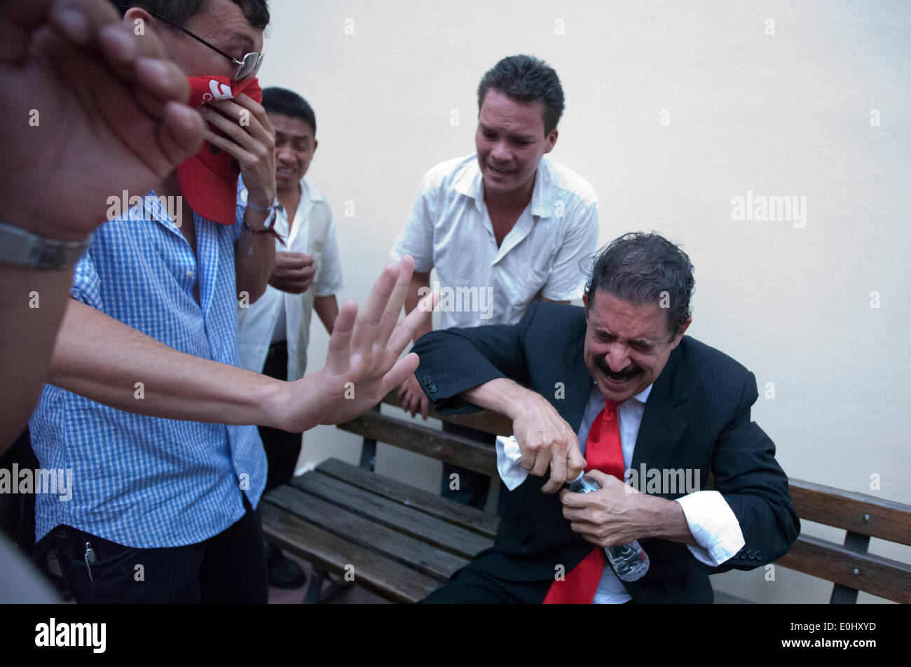 Tegucigalpa, Honduras. 13th May, 2014. The former Honduran President Manuel Zelaya (R) reacts after affected by tear gas and being evacuated with his followers from the National Congress, in Tegucigalpa, Honduras, on May 13, 2014. Followers and deputies of the Liberty and Refoundation Party (Libre, for its acronym in Spanish), the second political force in Honduras, broke in the National Congress on Tuesday, after clashing with police elements that guarded the Legislative Palace. Credit:  Rafael Ochoa/Xinhua/Alamy Live News Stock Photo