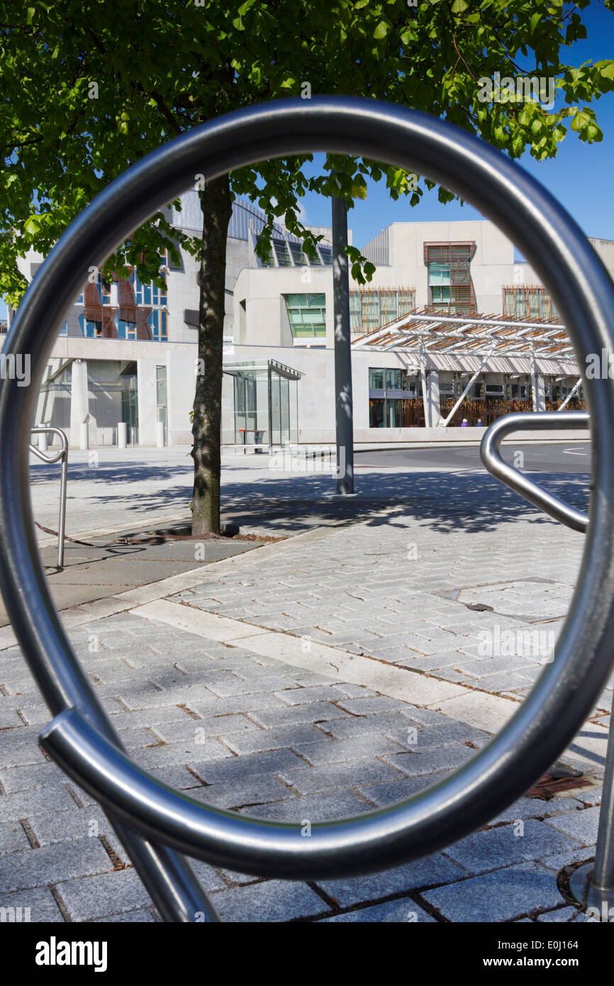 Scottish Parliament Building With Blue Sky And Green Foliage On Trees. Shot through circular bike rack. Stock Photo