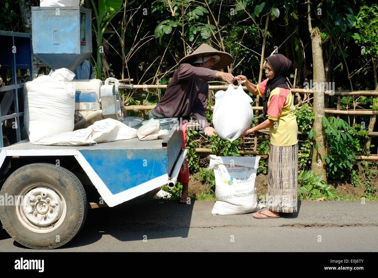 local man on a mobile rice sifting machine sells rice to village woman in java indonesia Stock Photo