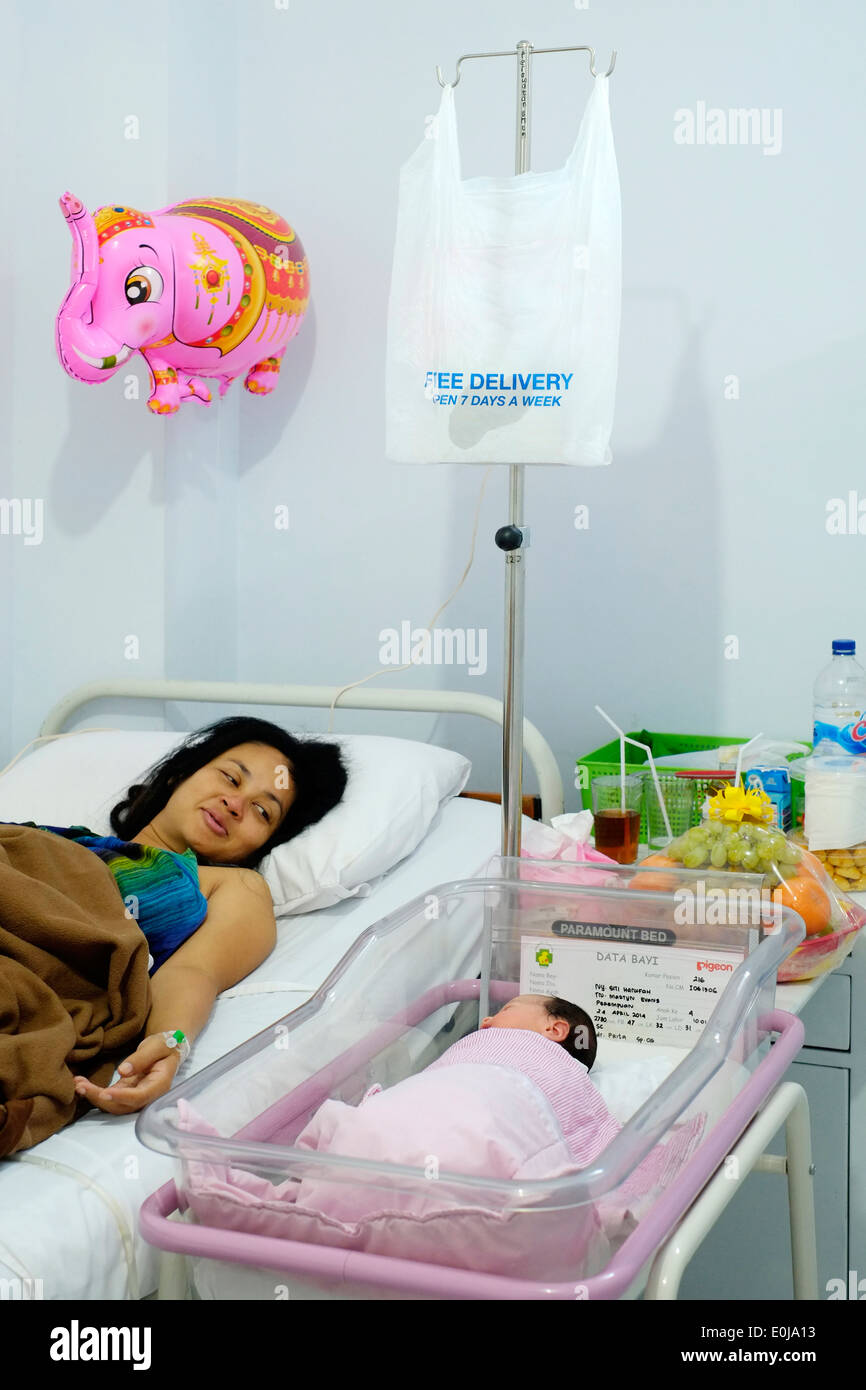mother proudly looks at her newly born sleeping daughter from her bed following cesarean in a hospital in malang indonesia Stock Photo