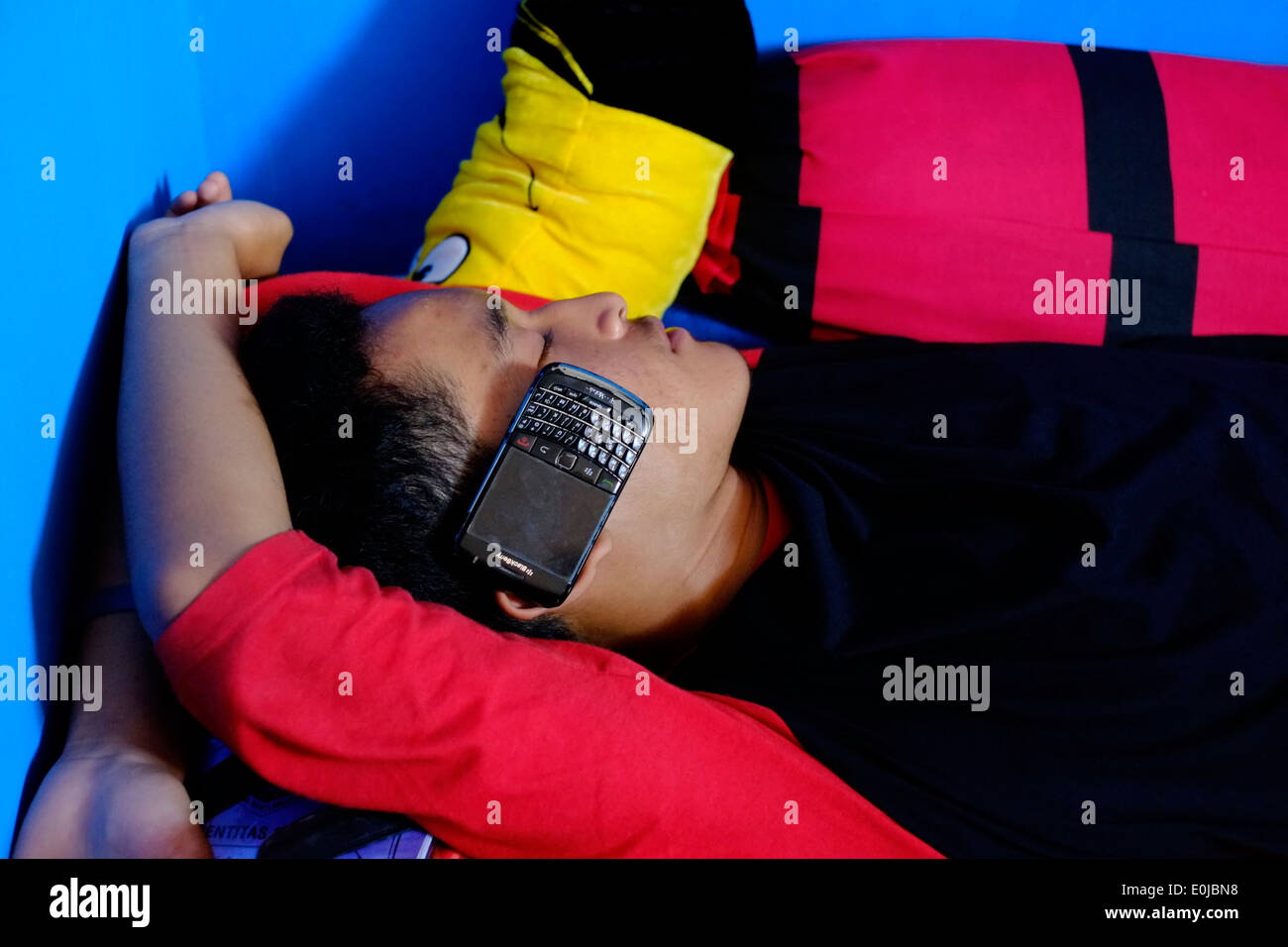 indonesian teenager sleeps whilst listening to music on his mobile phone east java indonesia Stock Photo