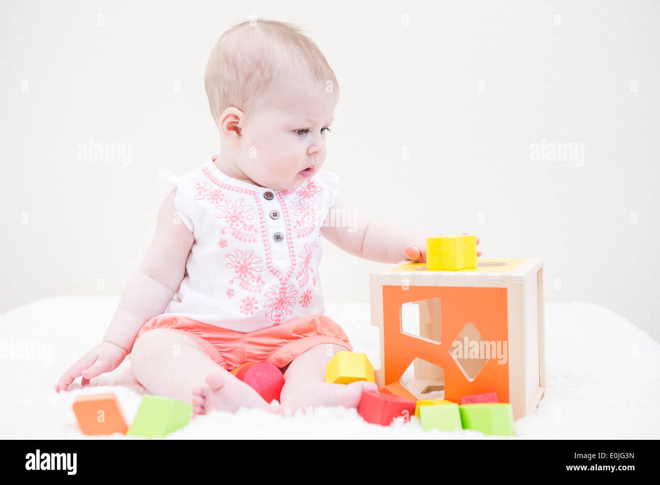 Baby girl playing with her toys on a white blanket Stock Photo - Alamy