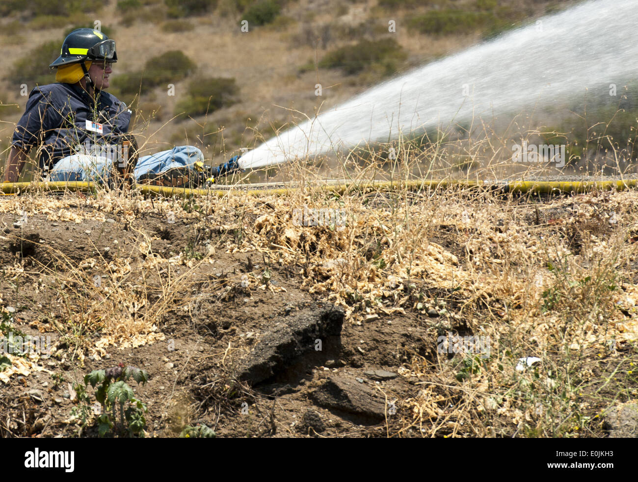 San Onofre, California, USA. 14th May, 2014. A San Onofre Nuclear Generating Station Fire Brigade member wets down vegetation just south of SONGS on Wednesday afternoon. Multiple Fire agencies, including Federal, State and County, responded to a wildfire on at the San Clemente Check Point that began when a truck on the northbound I-5 Freeway caught fire and passed to nearby vegetation on Wednesday morning. The Pendleton West Fire, had north and south bound trafficstopped, along with Amtrak Passenger Train traffic, as firefighters fought to contain the 150 plus acre fire that included water Stock Photo