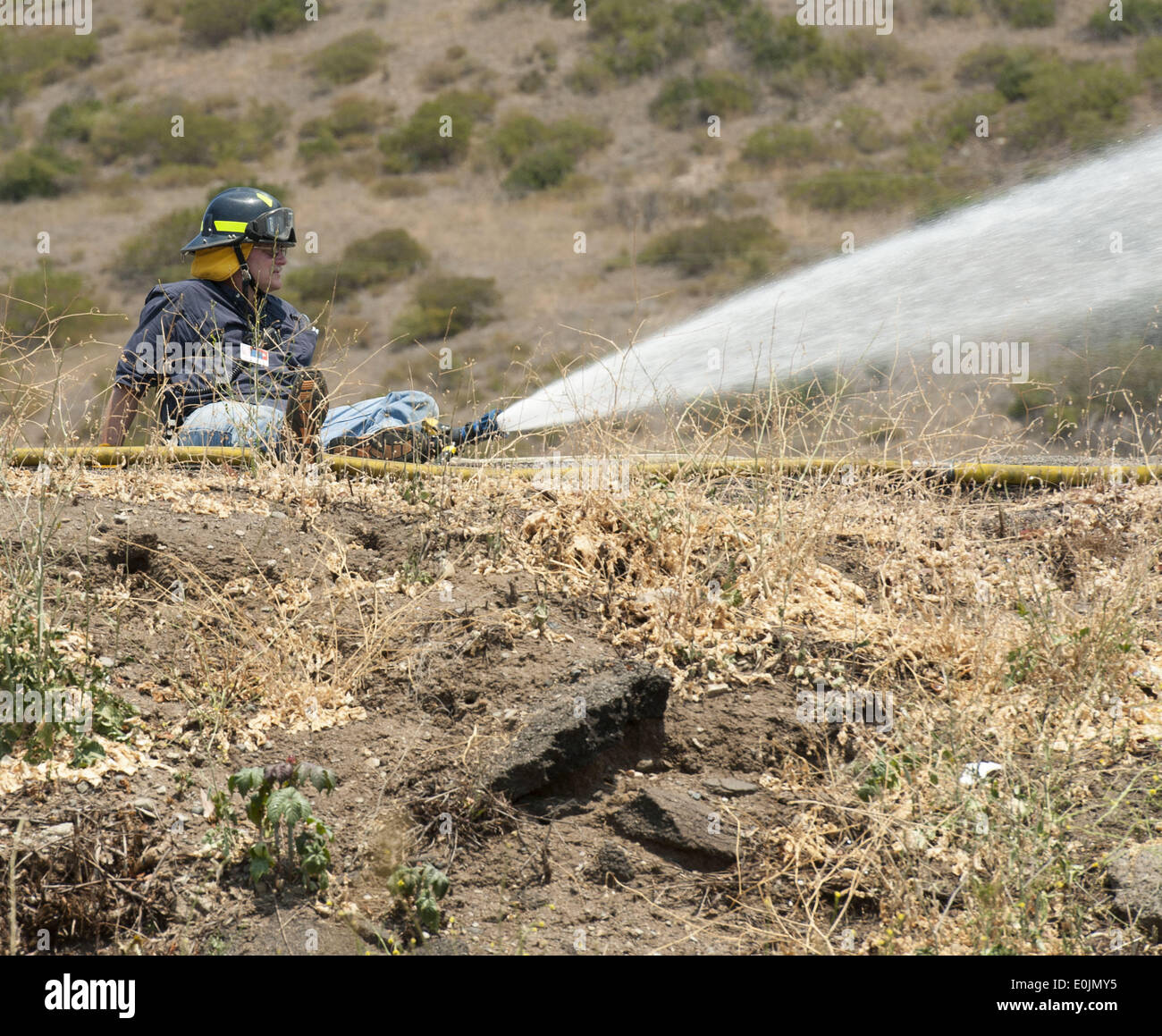 San Onofre, California, USA. 14th May, 2014. A San Onofre Nuclear Generating Station Fire Brigade member uses a fire hose to wet down surrounding vegetation on Wednesday morning. Multiple Fire agencies, including Federal, State and County, responded to a wildfire on at the San Clemente Check Point that began when a truck on the northbound I-5 Freeway caught fire and passed to nearby vegetation on Wednesday morning. The Pendleton West Fire, had north and south bound trafficstopped, along with Amtrak Passenger Train traffic, as firefighters fought to contain the 150 plus acre fire that include Stock Photo