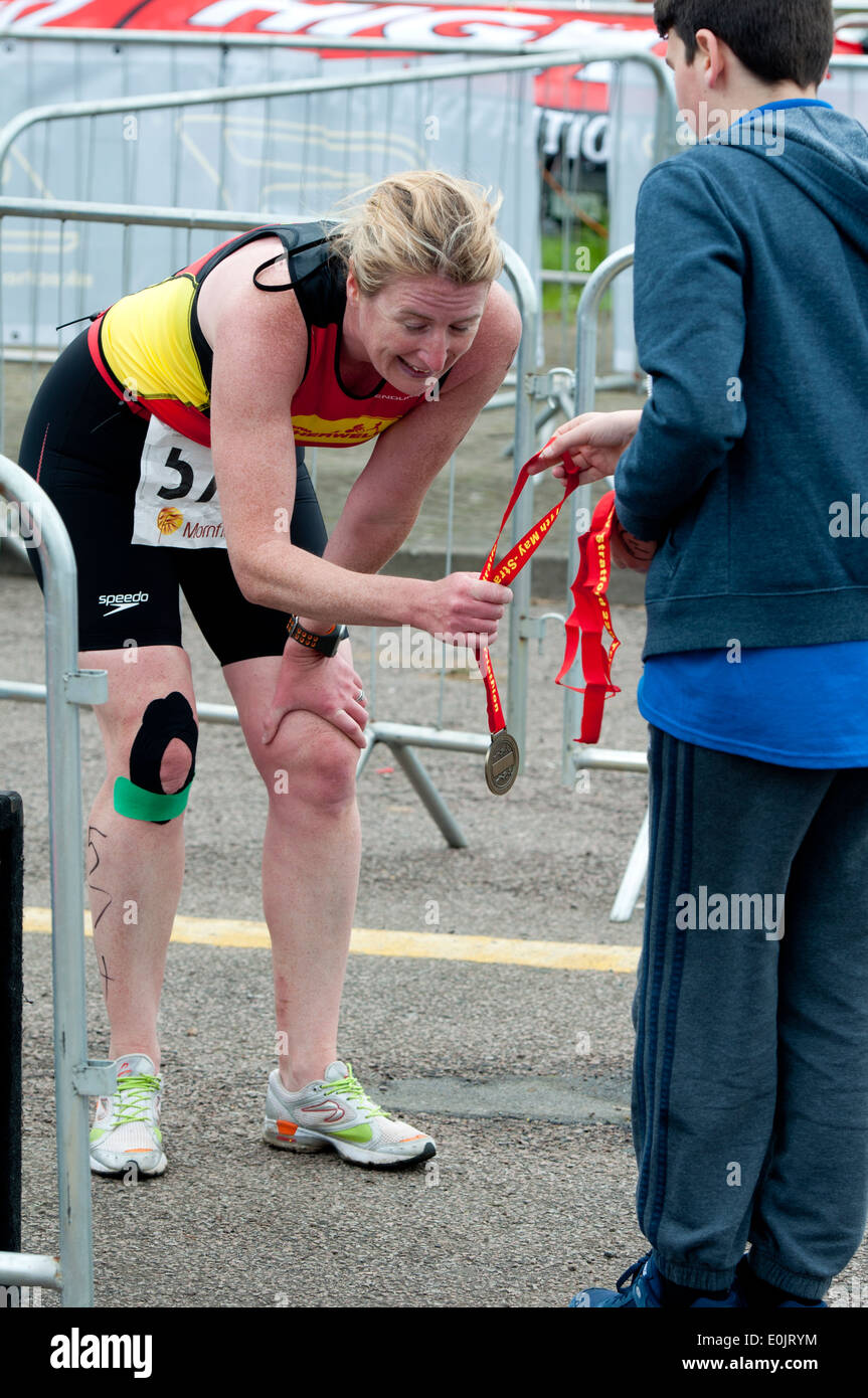 Stratford 220 Triathlon, exhausted female competitor at the finish of the race receiving her medal Stock Photo