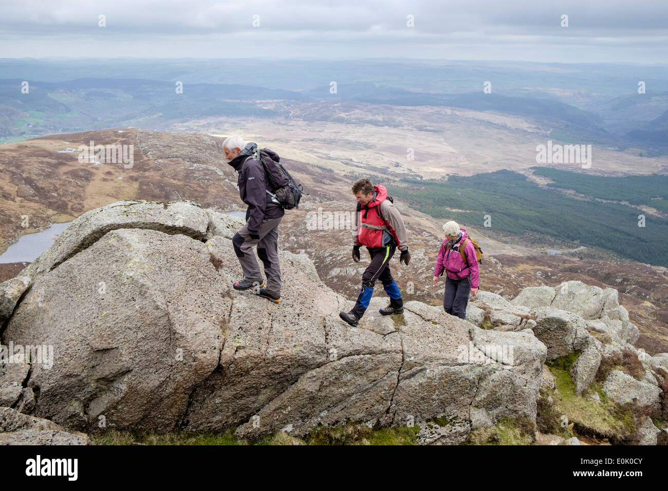 Three hikers scrambling over rocks on Carnedd Moel Siabod Daear Ddu ridge in mountains of Snowdonia National Park North Wales UK Stock Photo