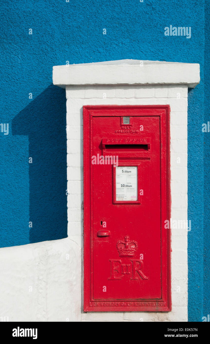 Bright Red Post Box on Bright Blue Painted Wall, Isle of Anglesey, North Wales, UK Stock Photo