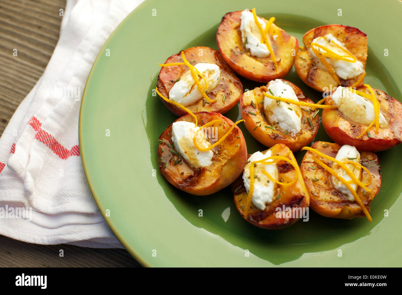 A plate of grilled peaches with creme fraiche, garnished with orange peels, chopped rosemary and balsamic vinegar. Stock Photo