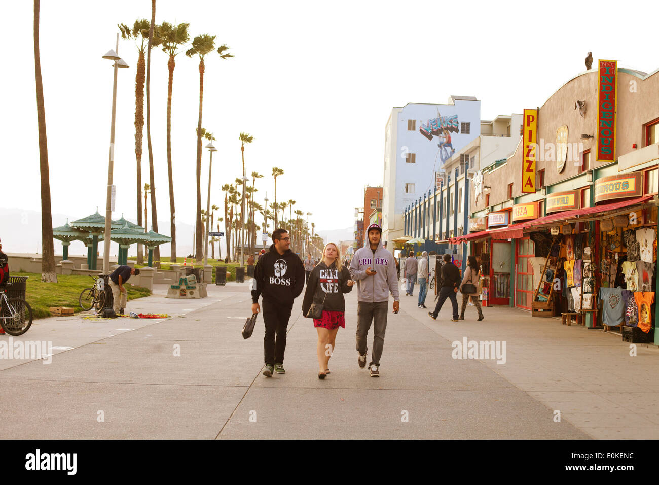Three friends walk down the sunny Venice Beach Boardwalk in Los Angeles