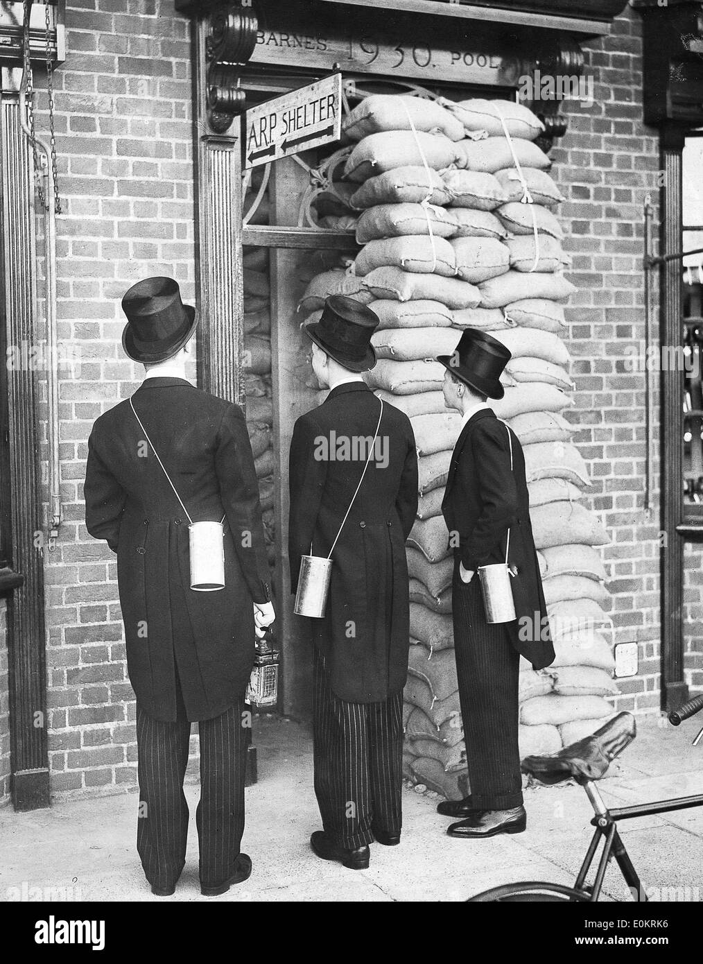 Here three boys, carrying gas masks, examine the sandbagged entrance to an air raid shelter. Stock Photo