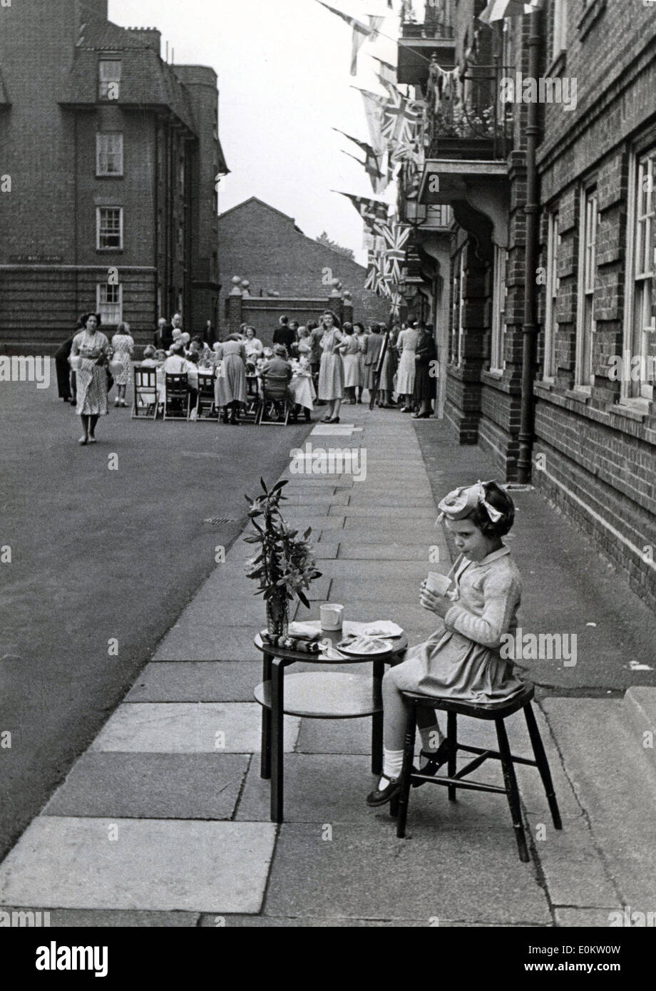 June 25, 1951 - London, England, U.K. - Young ANGELA LUFF age five, sadly sits 30 yards away from the Festival tea party for the children in Hortensia House, because she was diagnosed with chicken pox and not allowed to be near the other children. Stock Photo