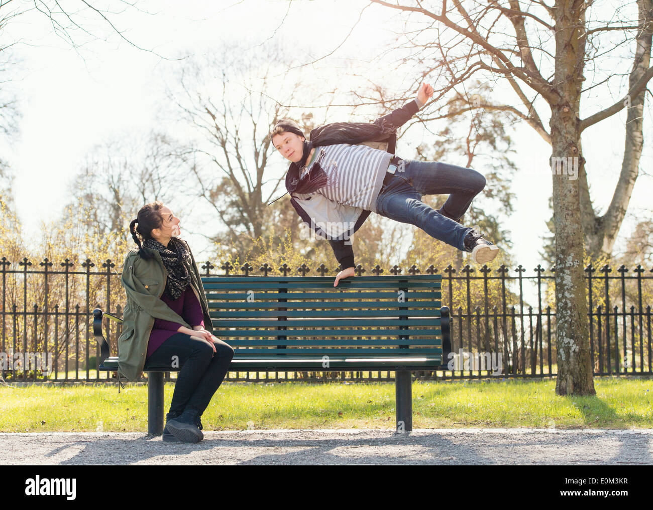Young man trying to impress indifferent girl by jumoing over a park bench Stock Photo
