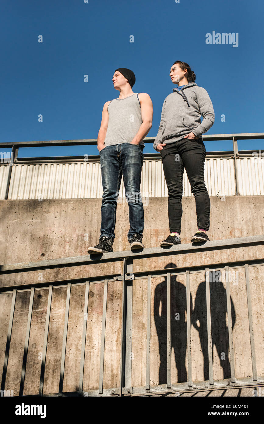 Portrait of casual and relaxed young man and woman balancing on rail in urban area. Stock Photo
