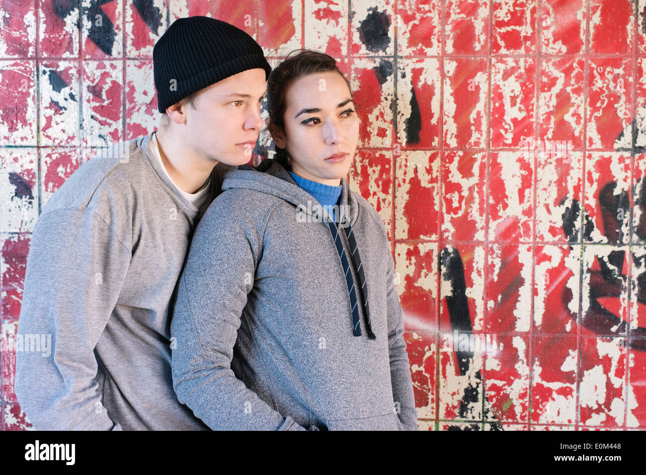 Portrait of casual and relaxed young man and woman waiting in front of grafitti wall in urban area. Stock Photo