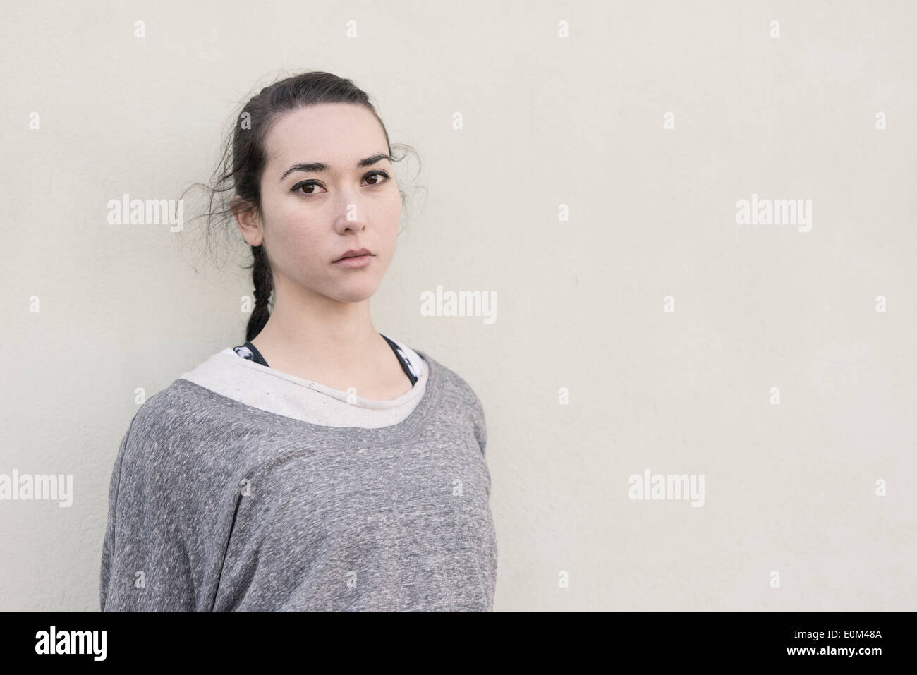 Portrait of young hispanic woman standing in front of wall. Pensive expression and looking at camera. Stock Photo
