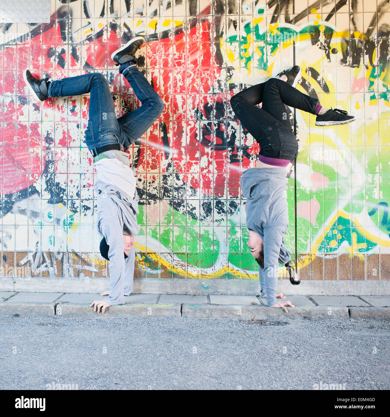 Portrait of young man and woman doing handstand in front of grafitti wall in urban area. Stock Photo