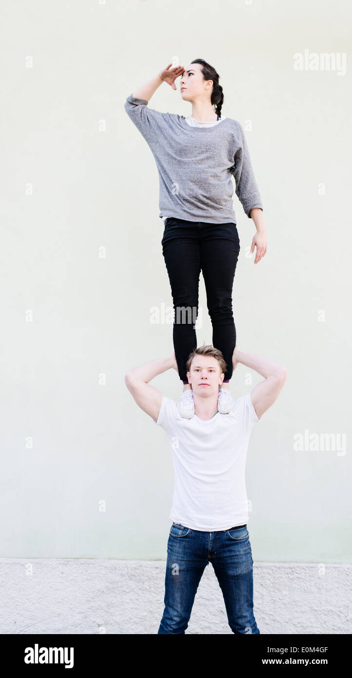 Woman standing on shoulders of man looking away, searching. Conceptual image of teamwork, support and vision. Stock Photo