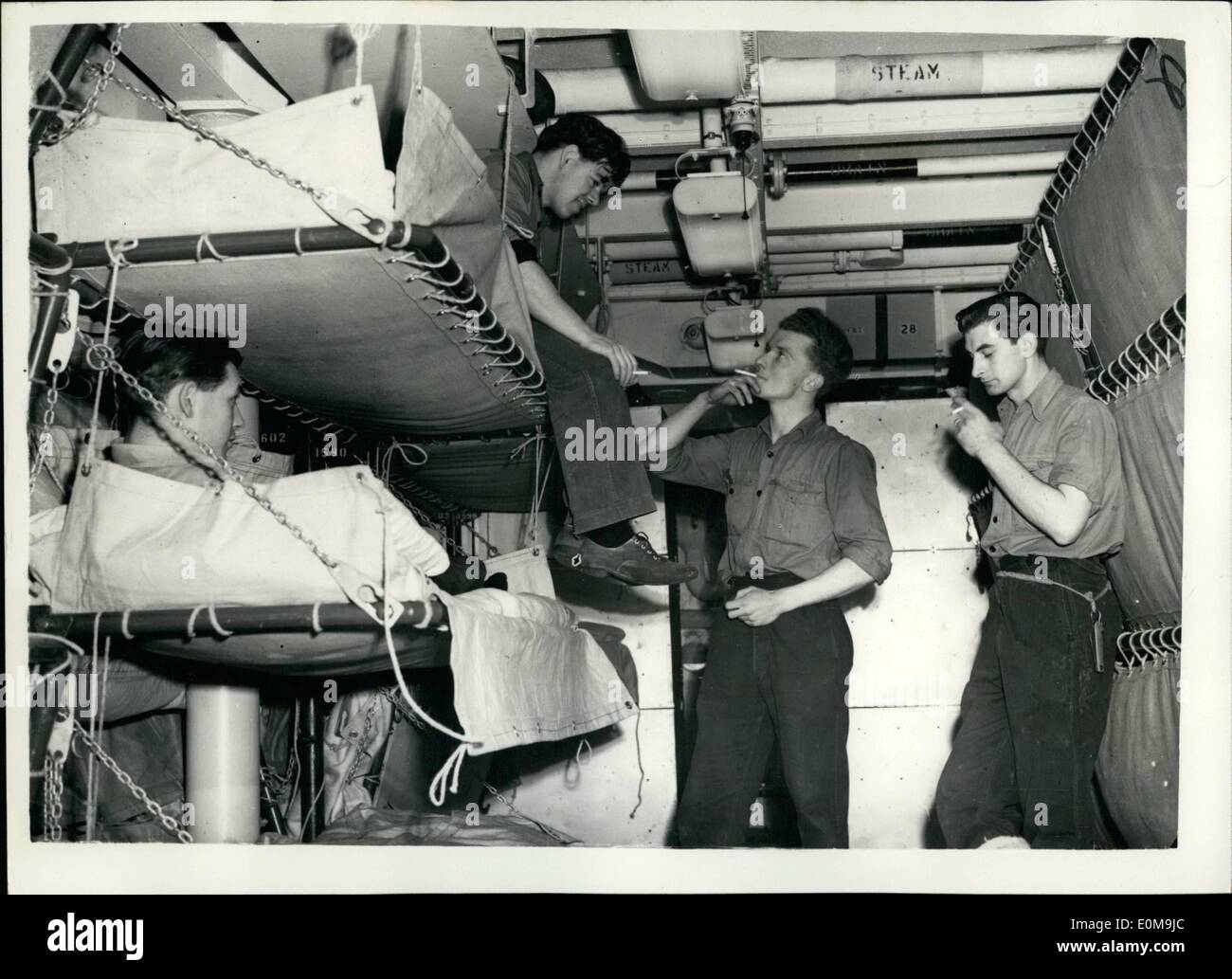 Apr. 04, 1954 - Canvas Bunks take Place of Hammocks in new British Aircraft Carriers.: To improve living conditions of ship's Companies - canvas bunks are to replace the traditional hammock in the two new aircraft carriers the Centaur and Albion. The bunks are so designed that they can be stowed when not in use and the extra space for which 'nests' of tables are provided - can be used for recreational purposes. Photo shows Scene in the Ordinary Seamen's mess deck - as two A.B's use the canvas bunks as they chat to colleagues whos bunks are stacked alongside the wall - aboard H.M.S Stock Photo
