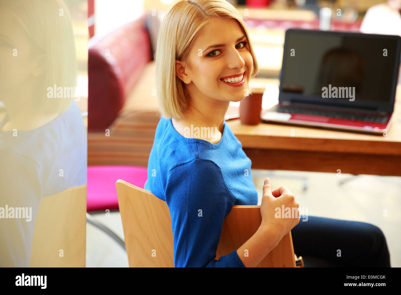 Young happy woman sitting at the table with laptop and looking at ...