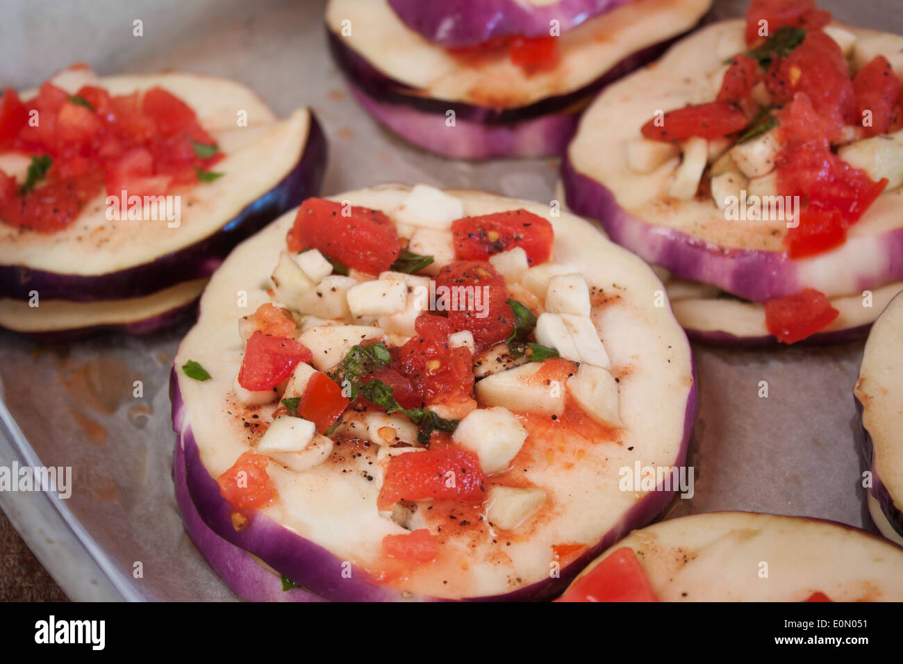 slices eggplant chopped tomato seasoning dressing spices dripping pan closeup Stock Photo