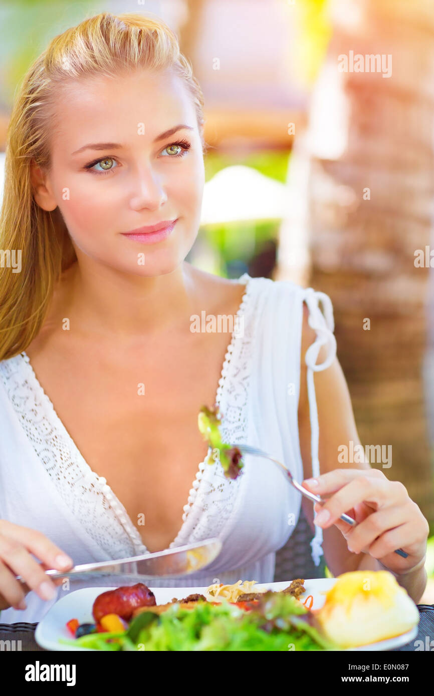 Portrait of attractive woman eating fresh salad and meat using knife