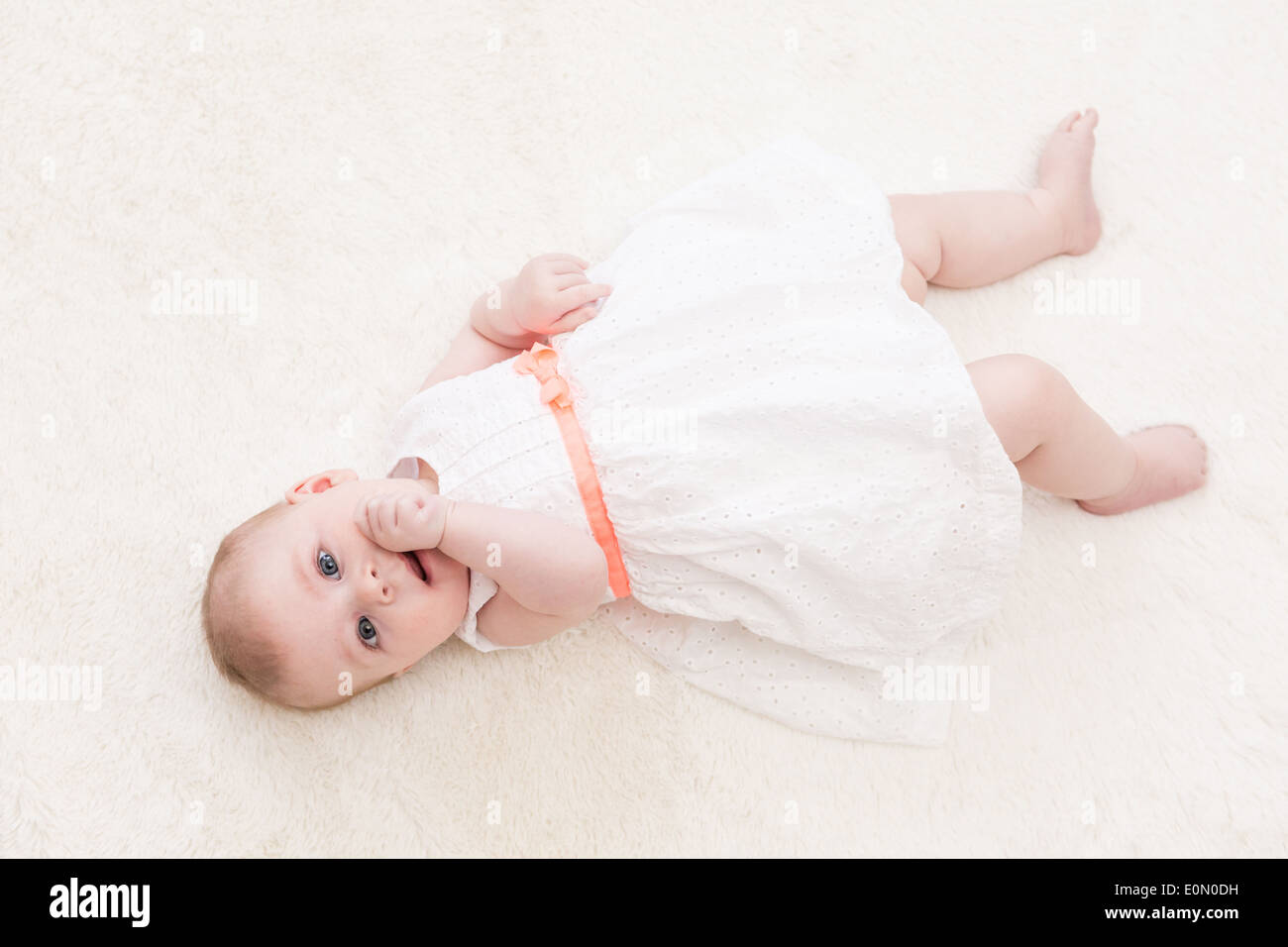 Baby girl in white dress playing on white blanket Stock Photo - Alamy